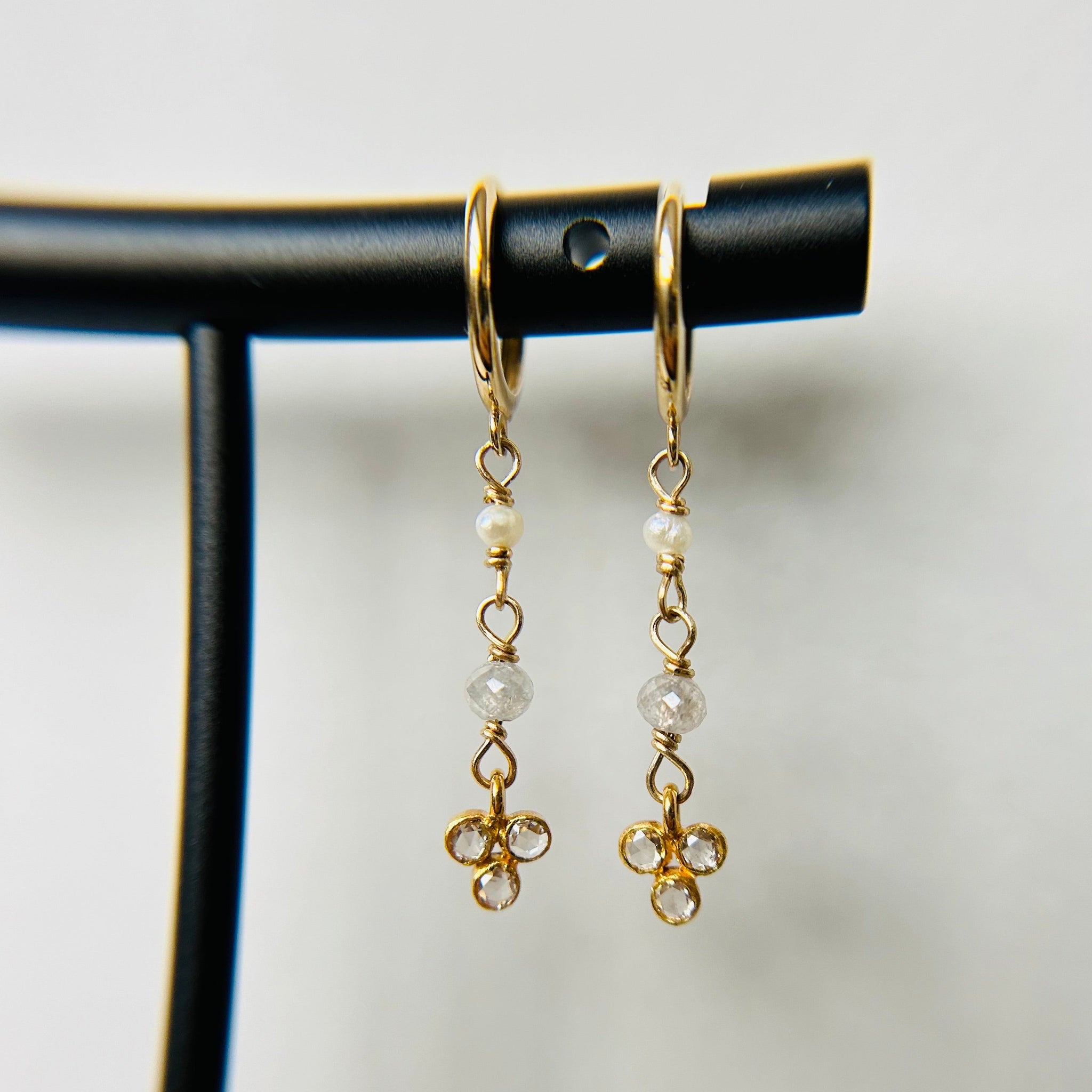 A pair of 14K gold hoop earrings with icy diamond and pearl dangles on a black display stand.