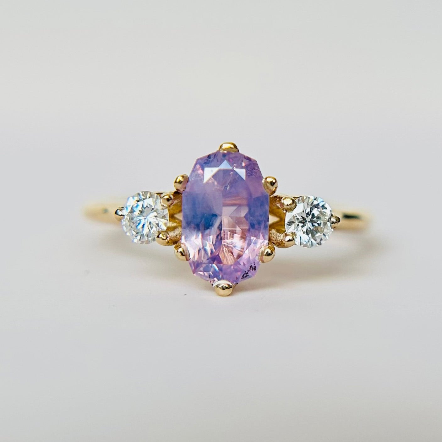 A lilac-hued sapphire ring with round diamond accent stones set in 14K yellow gold.
