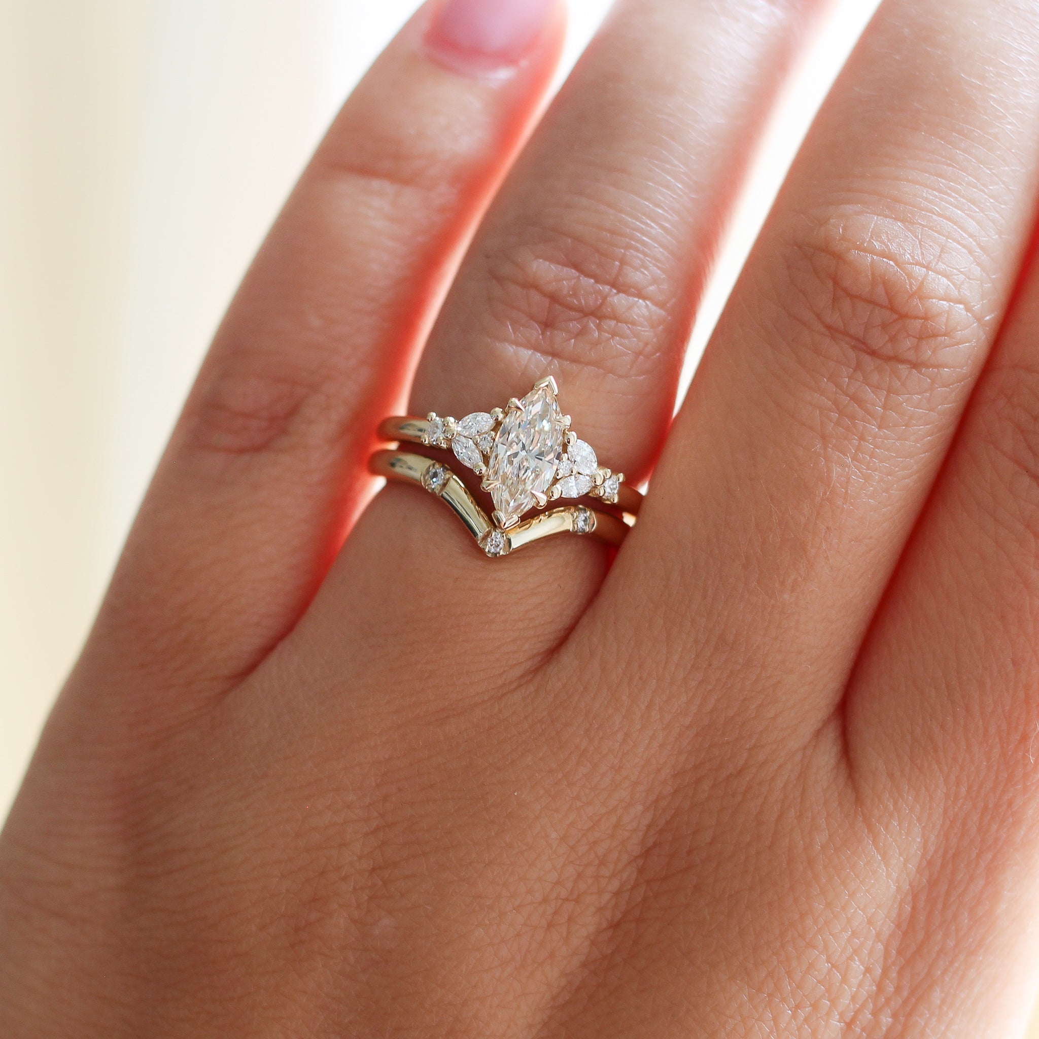 Yellow gold ring with a champagne marquise cut diamond and white diamond clusters stacked with pointed wedding band with three round white diamonds, on hand