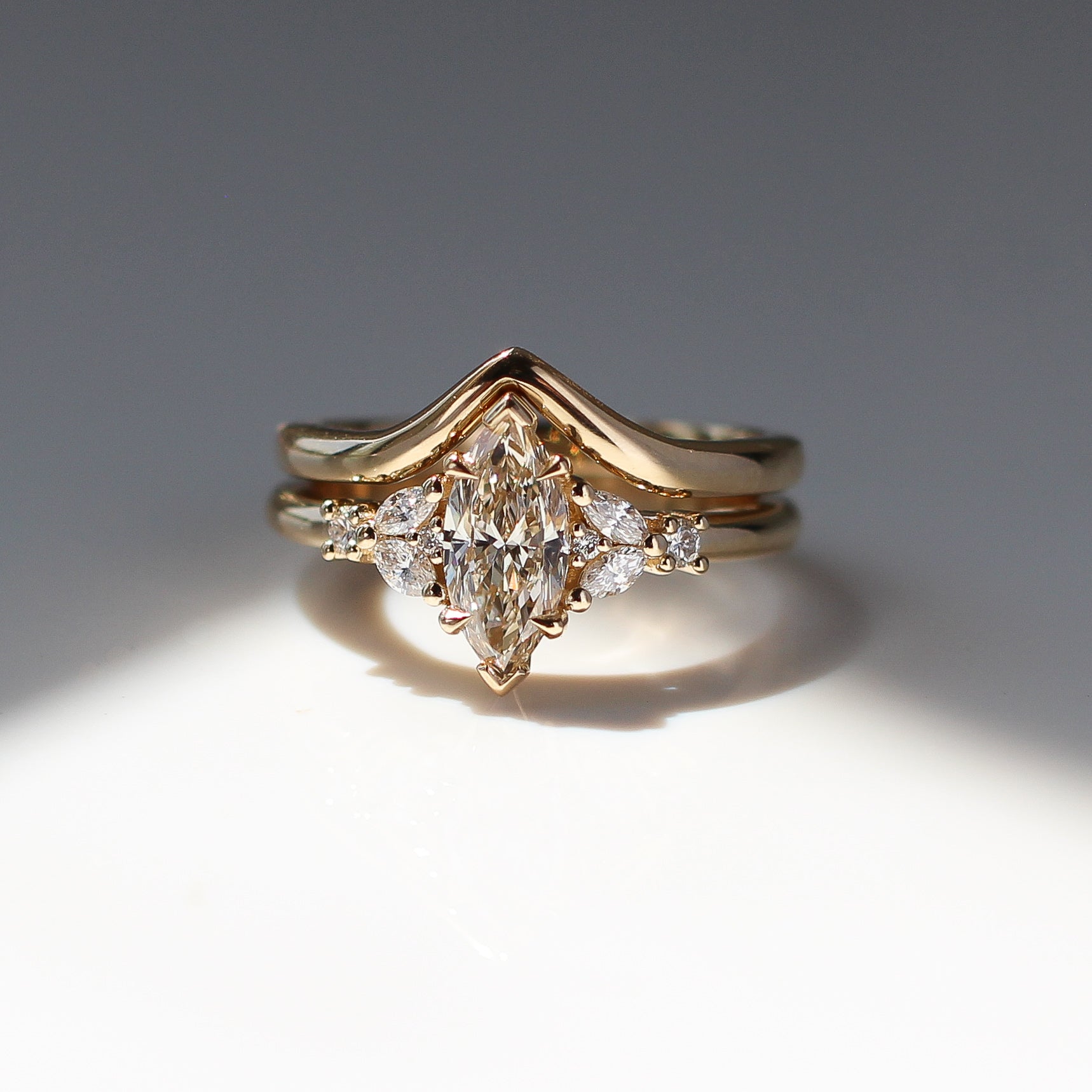 Yellow gold ring with a champagne marquise cut diamond and white diamond clusters stacked with pointed wedding band, front view