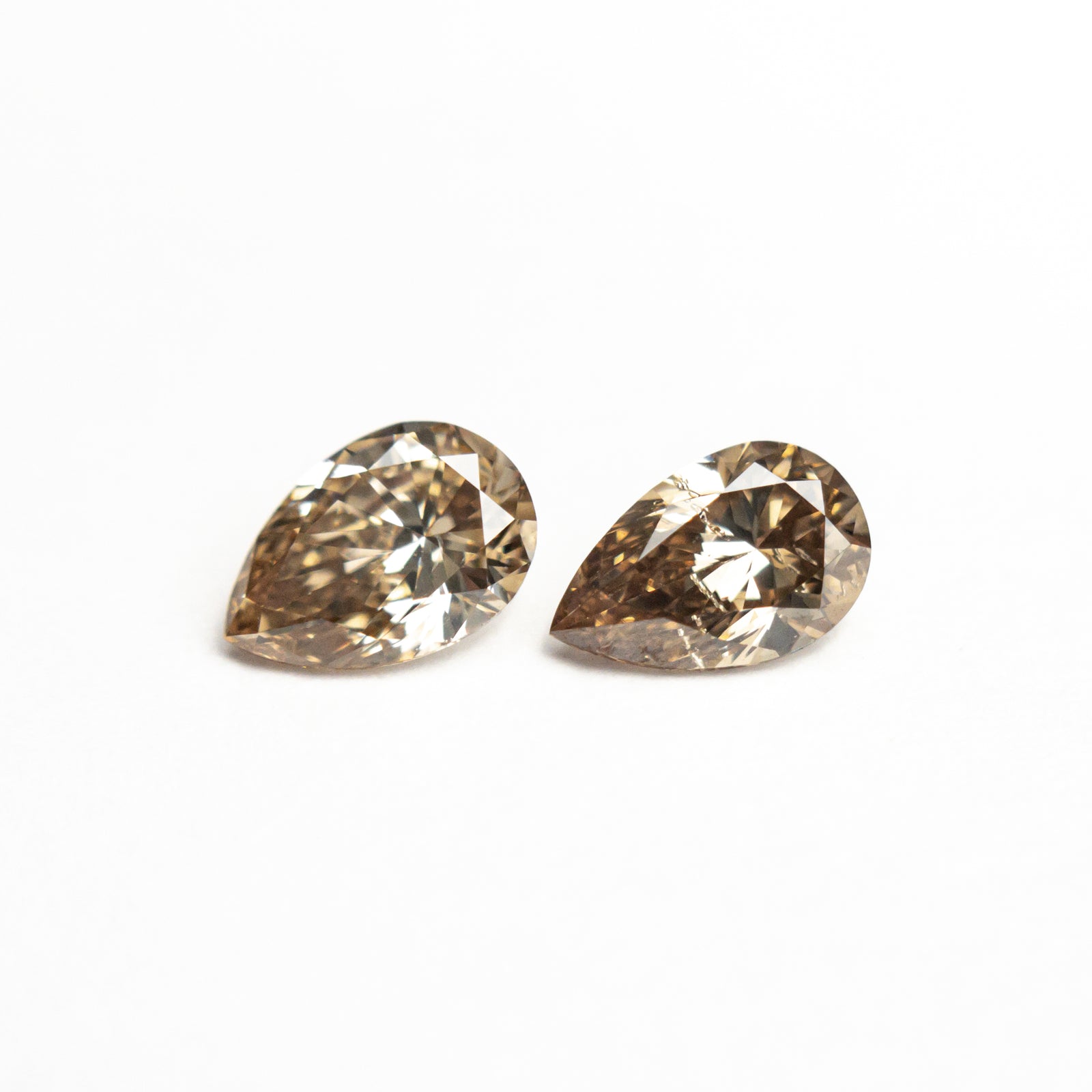 A pair of natural champagne diamonds with pear brilliant cut, side by side on a white background.