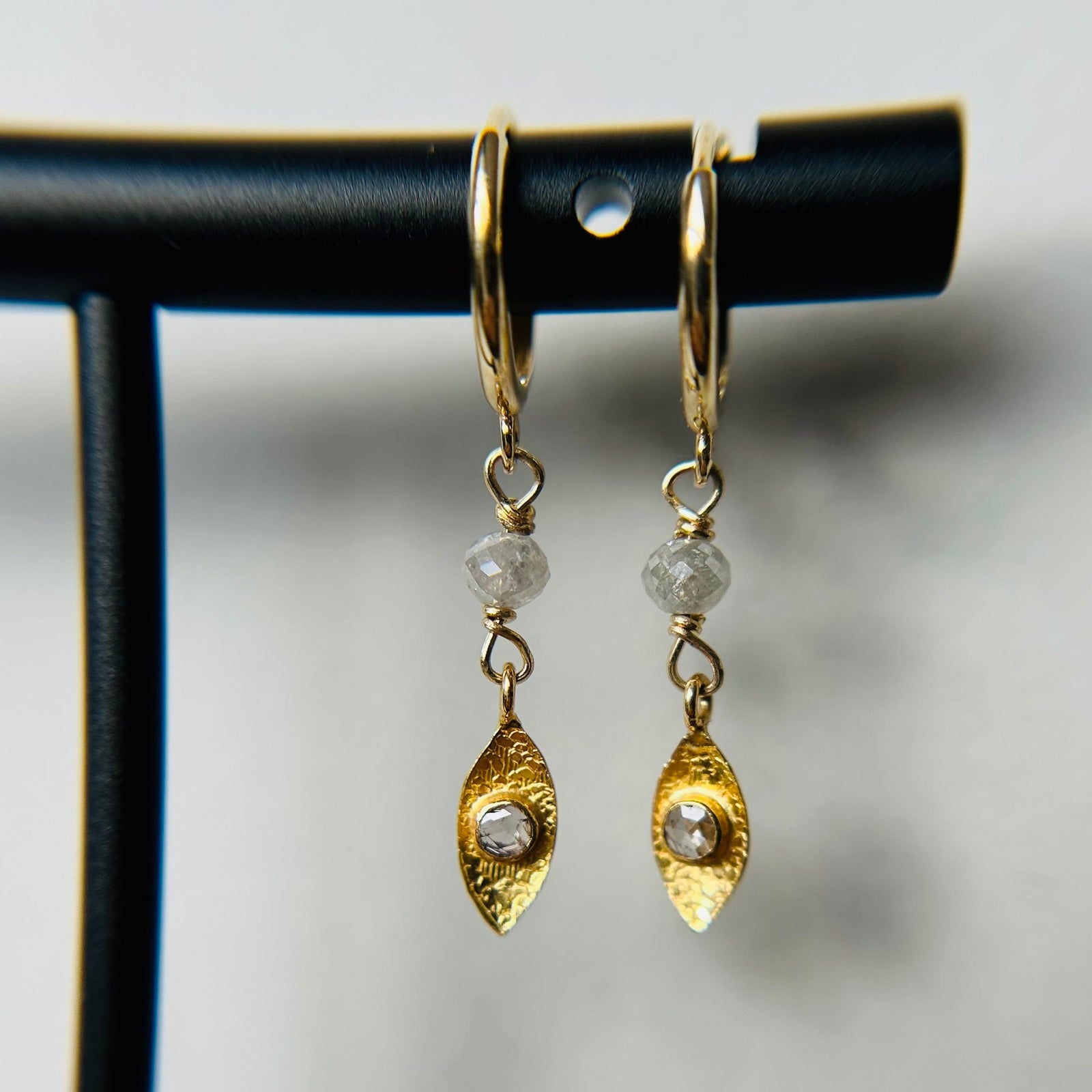 A pair of 14K gold hoop earrings with icy diamond accents displayed on a black stand.