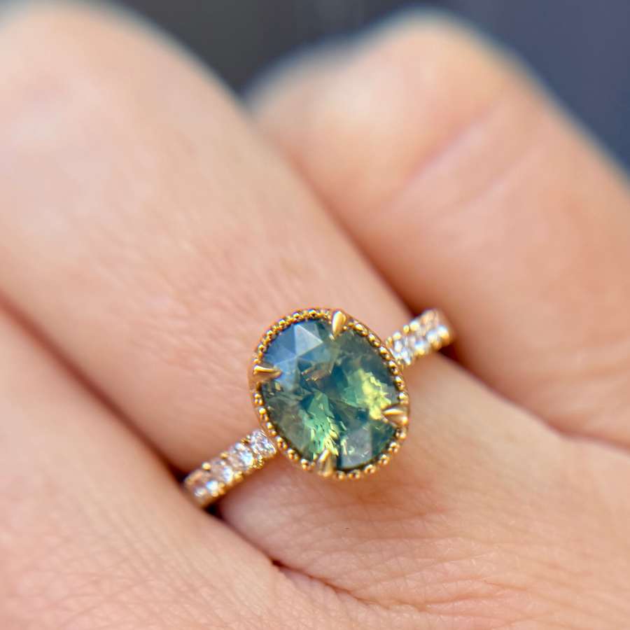 Yellow Gold engagement ring with a large teal oval gemstone, the light makes it glow on a gradient background