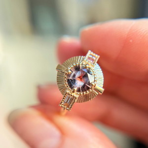 Gold engagement ring with a centre montana sapphire gemstone held between fingers against a blurred background