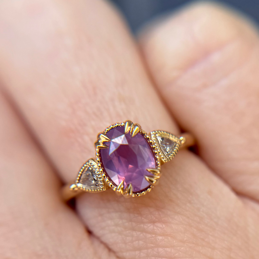 Yellow Gold engagement ring with a luminescent purple sapphire held by a hand against a pink background
