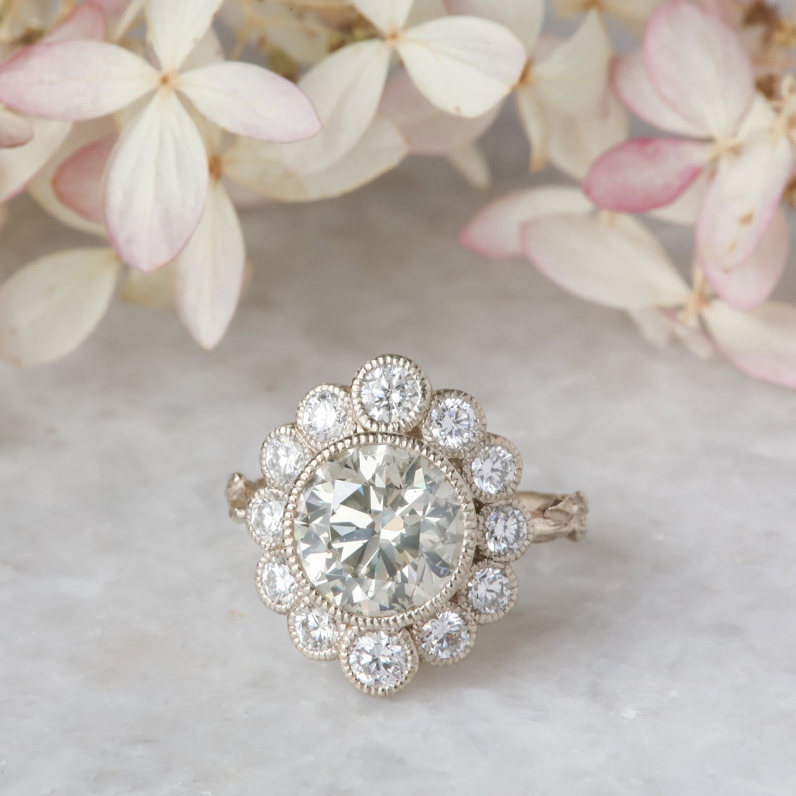 An antique inspired flower diamond halo engagement ring with natural light gray diamond center in white gold.