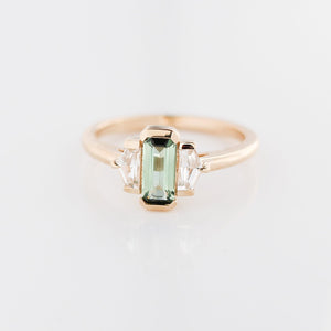 Three stone yellow gold ring, with elongated emerald cut green sapphire half bezel set and shield shaped white sapphire side stones in half bezel settings, front view