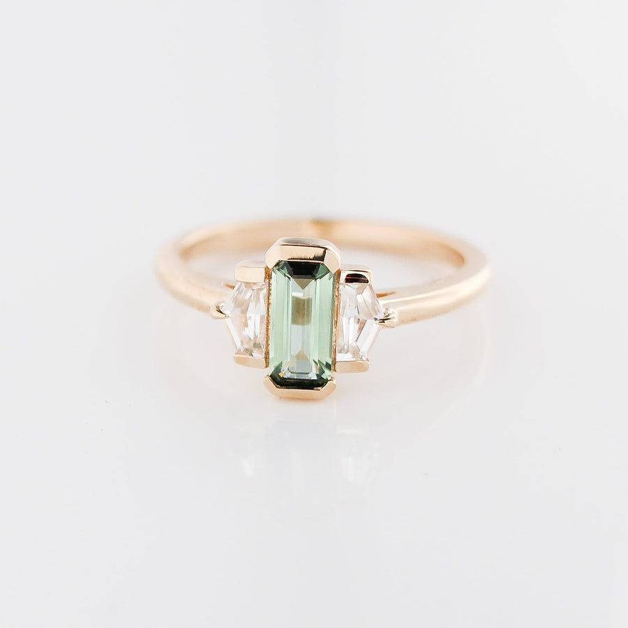 Three stone yellow gold ring, with elongated emerald cut green sapphire half bezel set and shield shaped white sapphire side stones in half bezel settings, front view