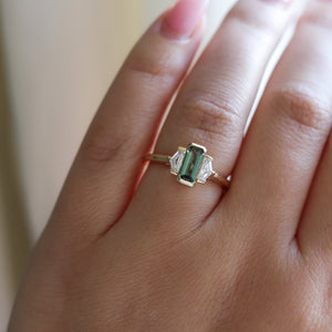 Three stone yellow gold ring, with elongated emerald cut green sapphire half bezel set and shield shaped white sapphire side stones in half bezel settings on hand, top view