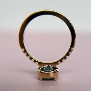 Yellow Gold engagement ring with a green sapphire gemstone shown upside down on a pink background to show the profile of the ring