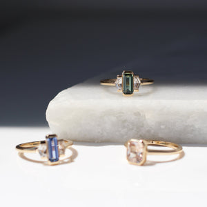 Three yellow gold engagement rings with coloured sapphires on a marble surface